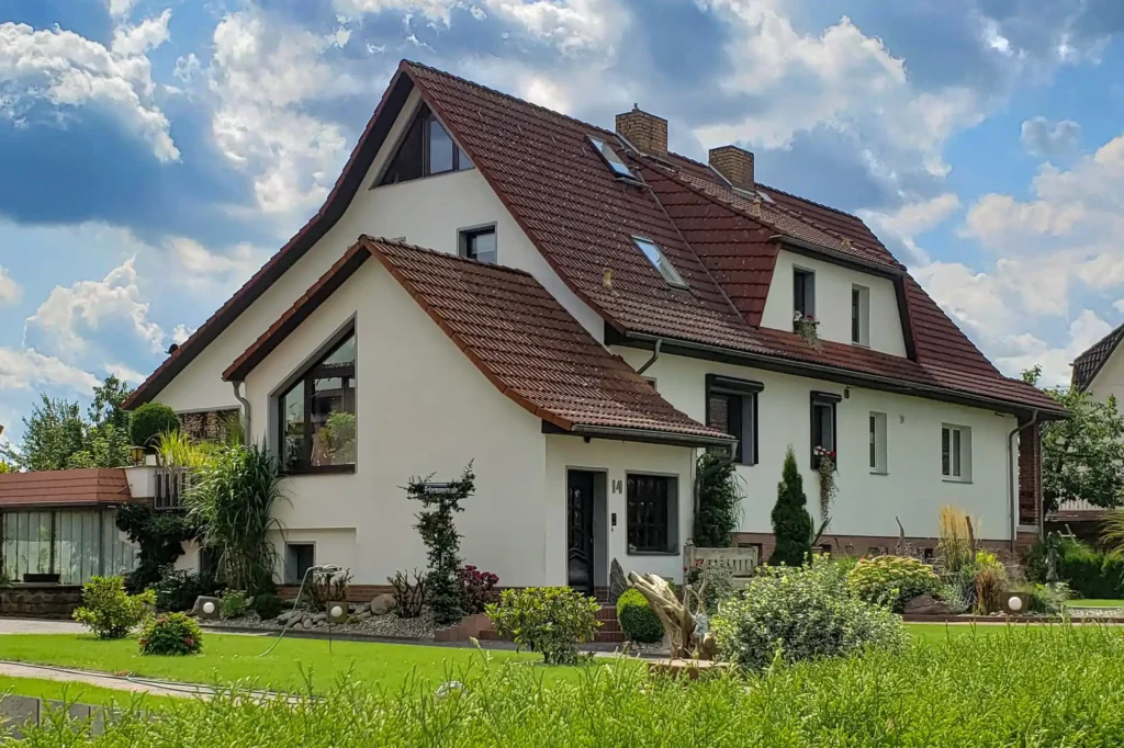Willkommen auf hausbauplan.com 5 Modernes Einfamilienhaus mit rotem Ziegeldach, gepflegtem Garten und klassischer Architektur bei sonnigem Wetter